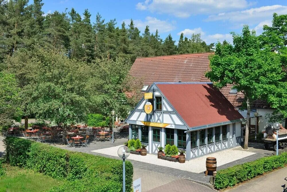Luftaufnahme vom kleinen Brauhaus umgeben von Bäumen und dem angrenzendem Biergarten mit Bestuhlung